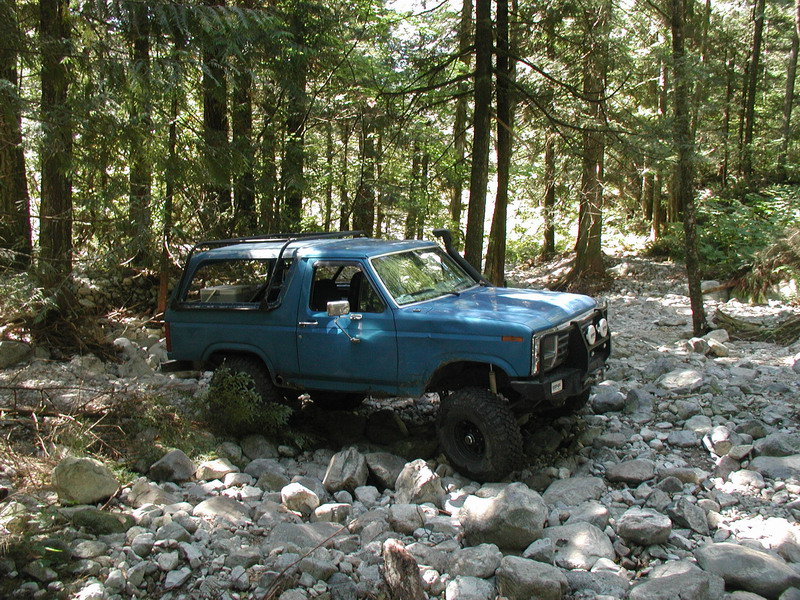 Blue Ford Bronco on a rocky forest trail.