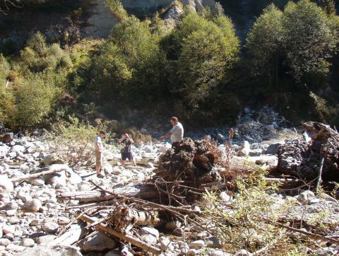 People in a rocky riverbed with trees and a steep embankment.