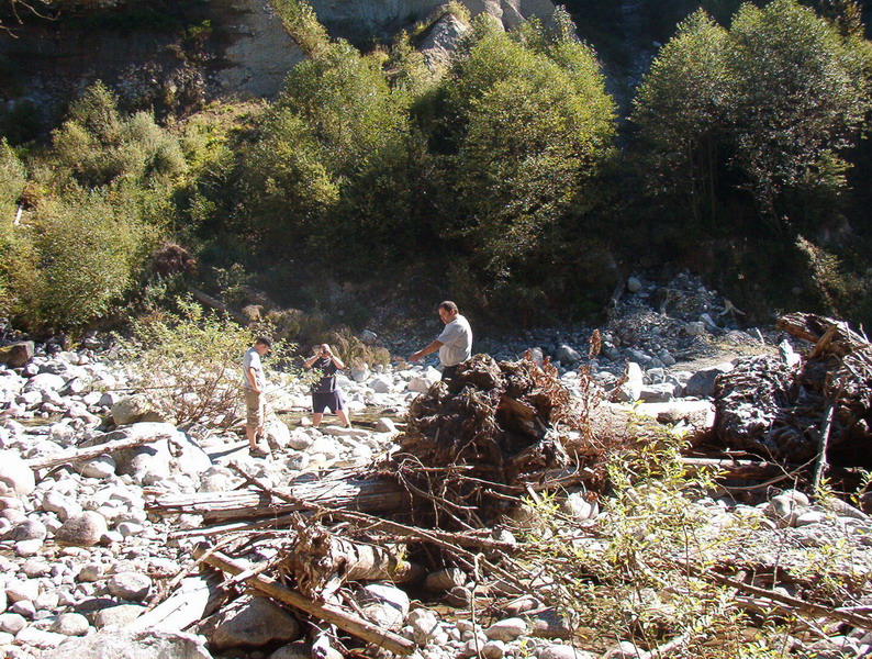 People in a rocky riverbed with trees and a steep embankment.