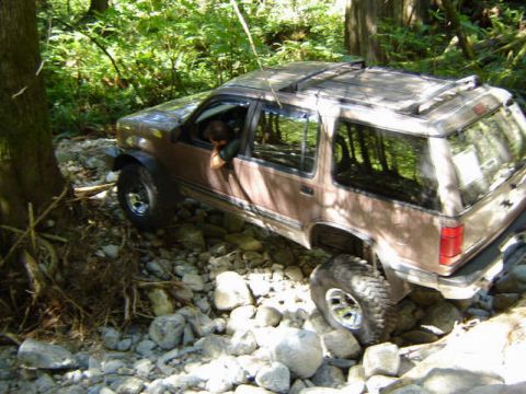 Brown SUV driving over rocks in a forest stream.