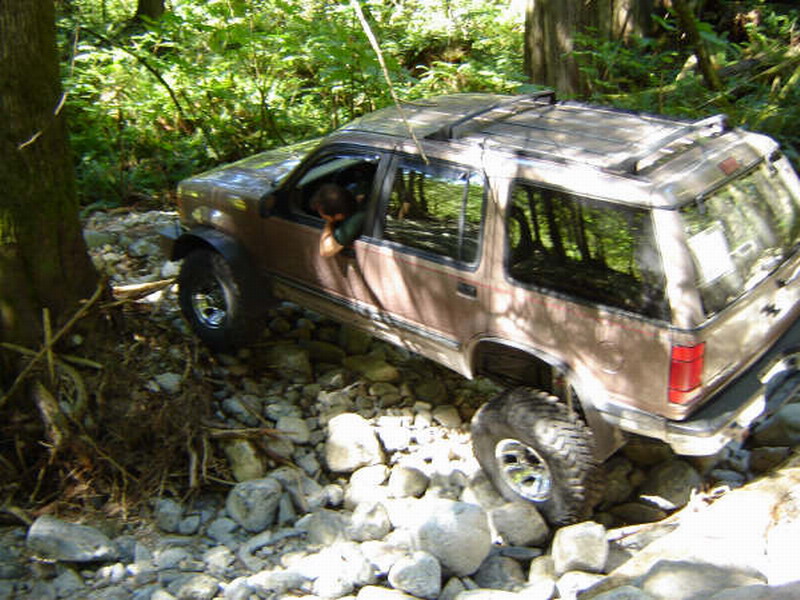 Brown SUV driving over rocks in a forest stream.