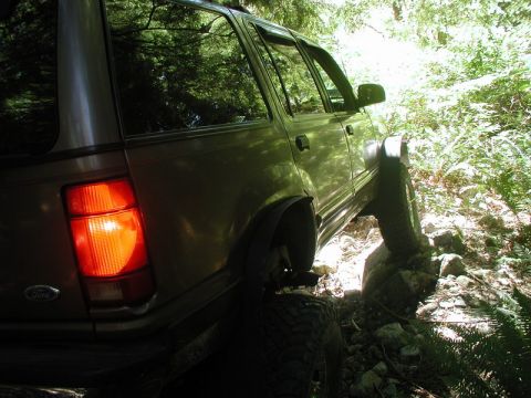 Tan SUV on a rocky trail, rear passenger side view.