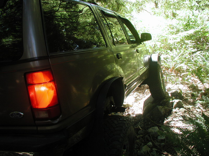 Tan SUV on a rocky trail, rear passenger side view.