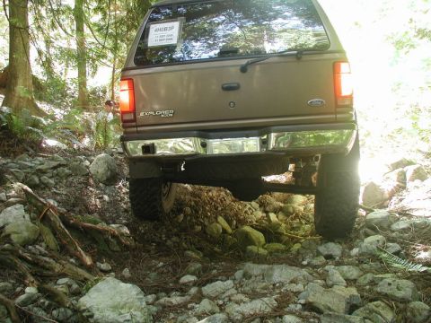 Rear view of a brown Ford Explorer on a rocky, wooded trail.