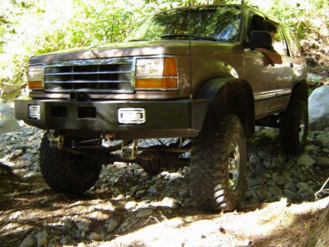 Lifted brown 4-door SUV with custom bumper and off-road tires on a rocky trail.