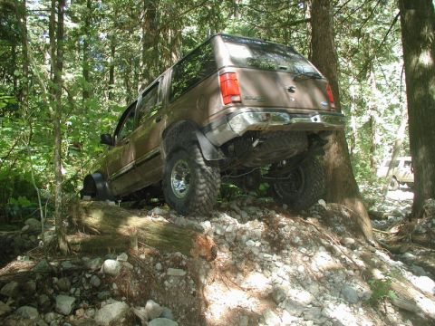 Brown SUV off-roading on a rocky, wooded trail.