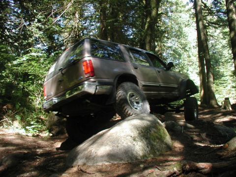 Lifted brown SUV off-roading on a rocky, wooded trail.