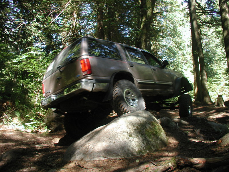 Lifted brown SUV off-roading on a rocky, wooded trail.