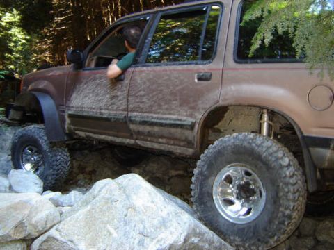Brown SUV off-roading on a rocky trail, front tire elevated on a rock.