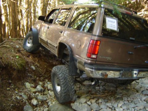 Brown Ford Explorer off-roading on a steep, rocky, wooded trail.