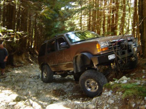 Brown Ford Explorer off-roading on a rocky trail in a forest.
