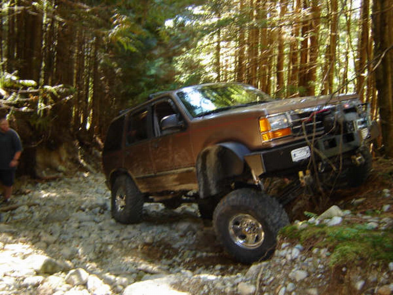 Brown Ford Explorer off-roading on a rocky trail in a forest.
