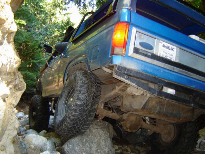 Blue Ford Bronco off-roading, rear passenger side view, tire on a rock.