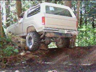 Tan 1980s Ford Bronco climbing a muddy hill off-road