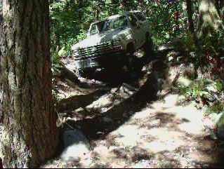 White 1985 Ford Bronco off-roading on a steep, wooded trail.