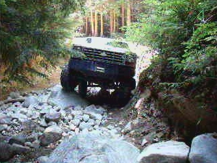 1985 Ford Bronco off-roading over rocks on a wooded trail