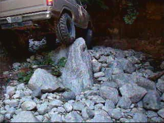Rear view of a tan SUV navigating a rocky obstacle course.