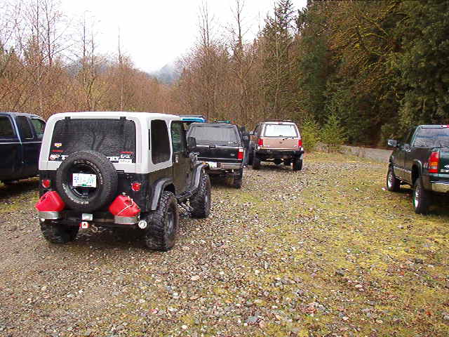 Rear view of a black and silver Jeep Wrangler with two red jerry cans on the bumper.
