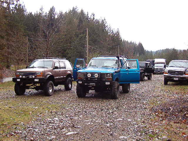 Several off-road SUVs and trucks parked on a gravel road, with a blue SUV in the foreground.