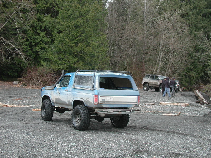 Lifted blue Ford Bronco with snorkel on a gravel beach.