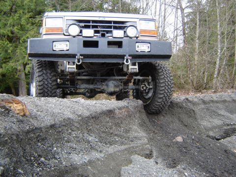 1985 Ford Bronco - A lifted, off-road modified Ford Bronco is positioned at an angle on a dirt embankment, with its front tires on the edge of the drop-off. T…