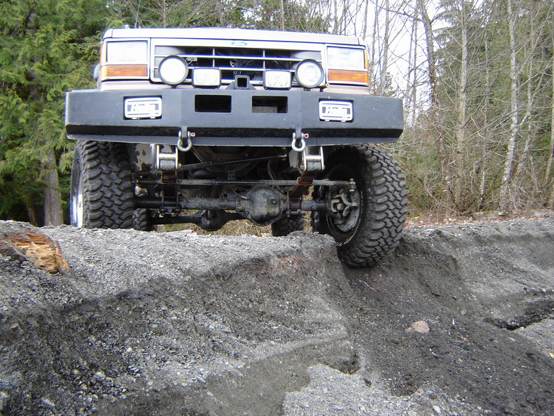 Lifted 1985 Ford Bronco off-roading on a dirt embankment.