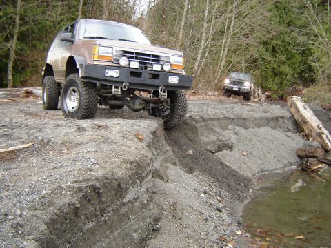 1985 Ford Bronco - A lifted, modified Ford Explorer is positioned on the edge of a steep dirt embankment next to a body of water. Another Ford Explorer is vis…