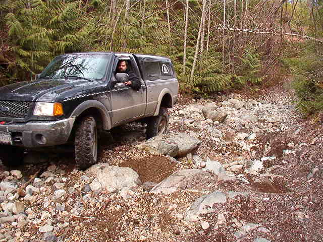 Black Ford Ranger pickup truck on a rocky, wooded trail.