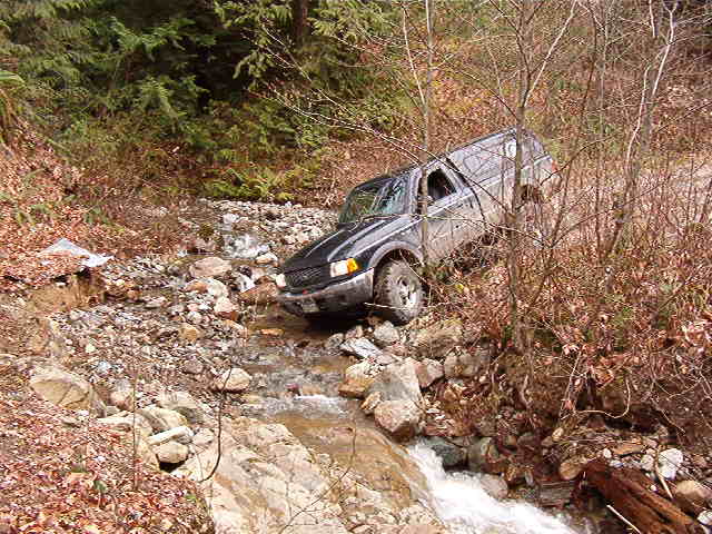 Black SUV driving through a rocky stream.