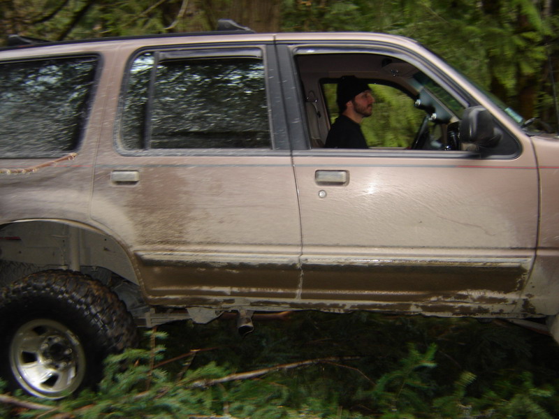 Tan SUV covered in mud driving through a forest.