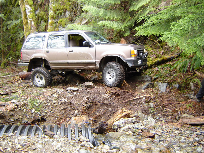 Lifted tan Ford Explorer on a muddy forest trail.