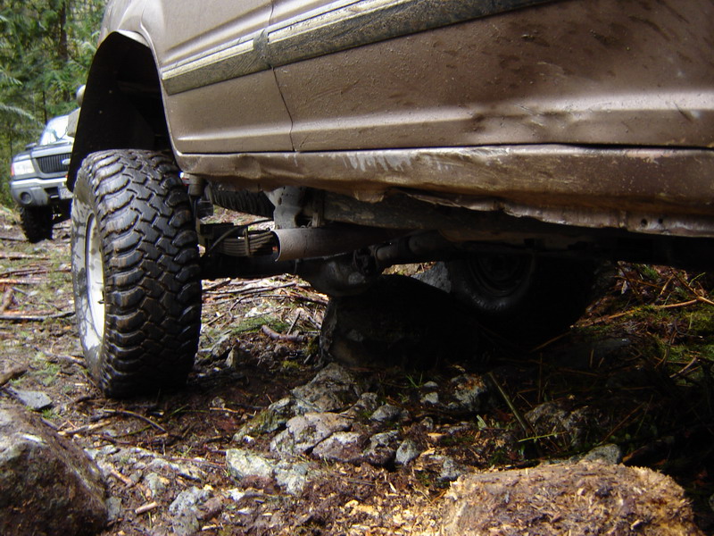 Close-up of a lifted off-road vehicle's undercarriage and tire on a rocky trail.
