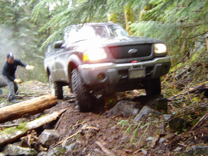 Ford pickup truck driving over rocks on a wooded trail.