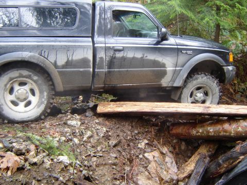 1985 Ford Bronco - A dark-colored Ford Ranger pickup truck is navigating an obstacle course, with its front tire on a makeshift bridge of logs and its rear ti…