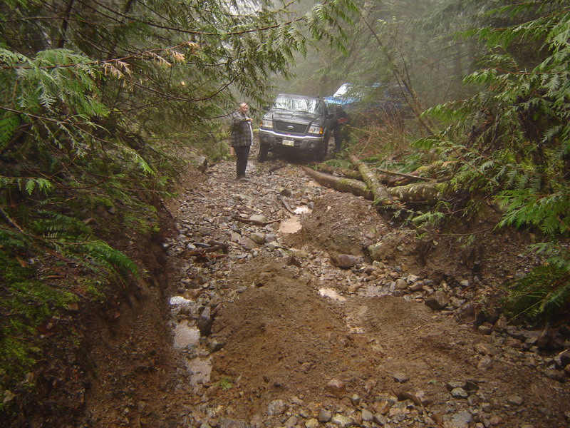 Off-road vehicles stuck on a muddy, rocky forest trail.