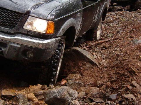1985 Ford Bronco - A black Ford pickup truck is navigating a rocky, off-road terrain, with its front passenger side tire angled up a large rock.