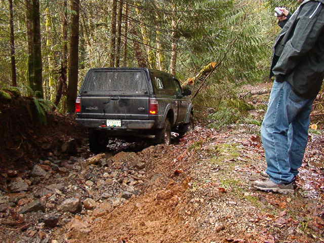Black Ford pickup truck on a muddy forest trail with a person taking a photo.