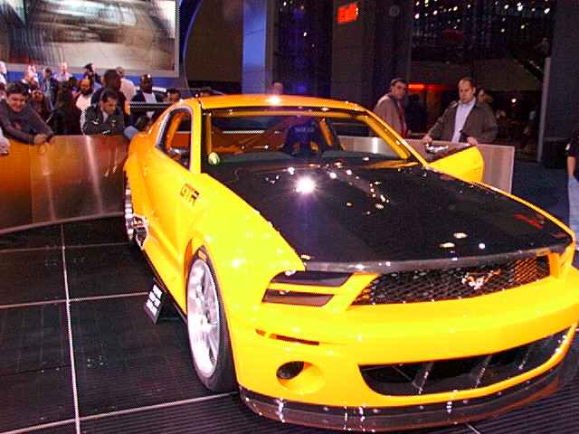 Yellow Mustang GT-R concept with black hood on a turntable at an auto show
