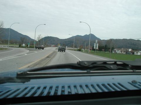 1985 Ford Bronco - A view from inside a vehicle looking out at a highway intersection with mountains in the background. Two SUVs are visible on the road, one…