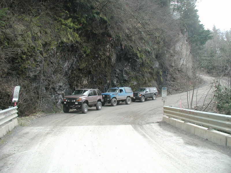 Three off-road vehicles parked on a gravel road next to a rocky embankment.