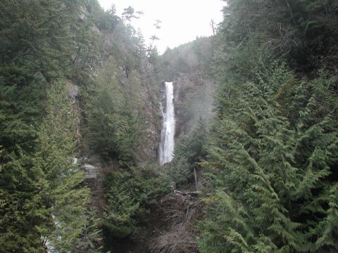 1985 Ford Bronco - A tall waterfall cascades down a rocky cliff face, surrounded by dense evergreen trees.