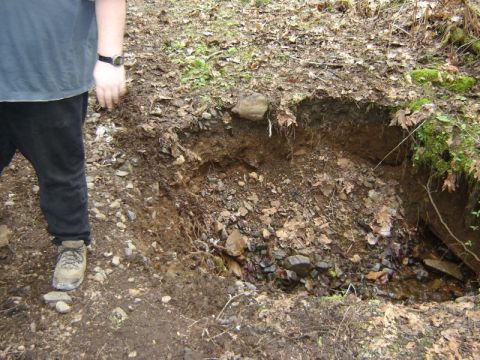 1985 Ford Bronco - A person stands next to a hole dug into the side of a dirt embankment. The hole reveals layers of soil and rocks, with a small stream of wa…