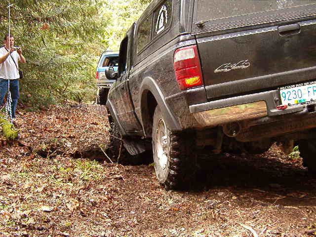 Off-road pickup truck driving on a dirt path with a camper shell.