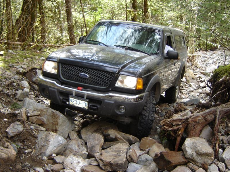 Black Ford pickup truck with camper shell driving on a rocky forest trail.