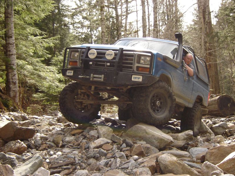 Blue 1980s Ford Bronco off-roading over rocks with a snorkel and brush guard.