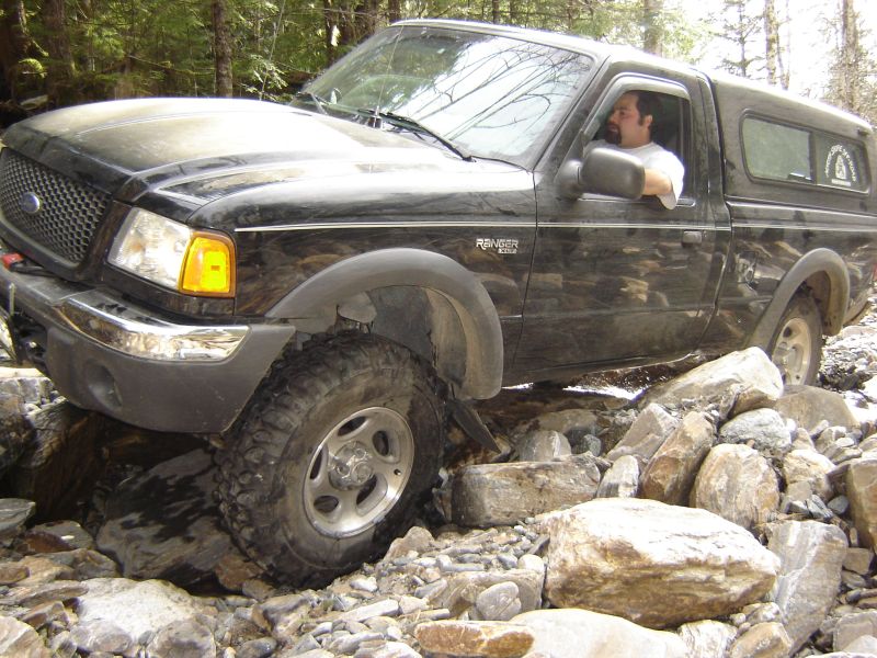 Black Ford Ranger pickup truck driving over rocks on an off-road trail.