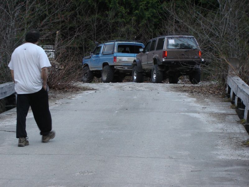 Man walking on bridge towards blue and brown off-road SUVs