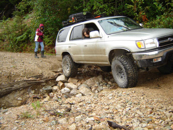 Silver SUV with off-road tires and roof rack on a rocky trail.