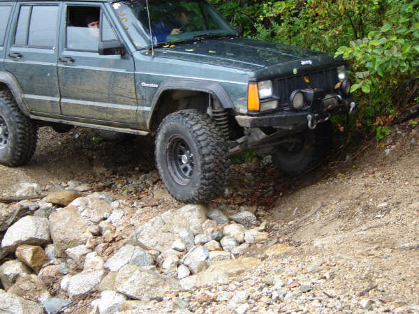 Dark green Jeep Cherokee climbing over rocks on an off-road trail.