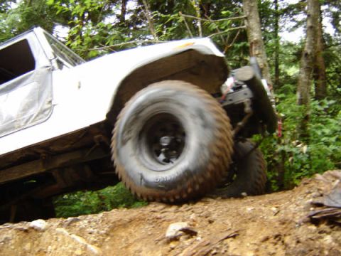1985 Ford Bronco - A white off-road vehicle is navigating a steep dirt incline with large, aggressive tires. The vehicle is tilted at an angle, showcasing its…